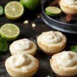 A close-up of mini no-bake key lime pies with golden crusts, topped with fresh whipped cream and lime slices, beautifully arranged on a white plate.