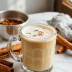 A steaming mug of vanilla cinnamon latte topped with whipped cream and a sprinkle of cinnamon, placed on a rustic wooden table with cinnamon sticks and vanilla beans around, evoking warm comfort and rich flavors.